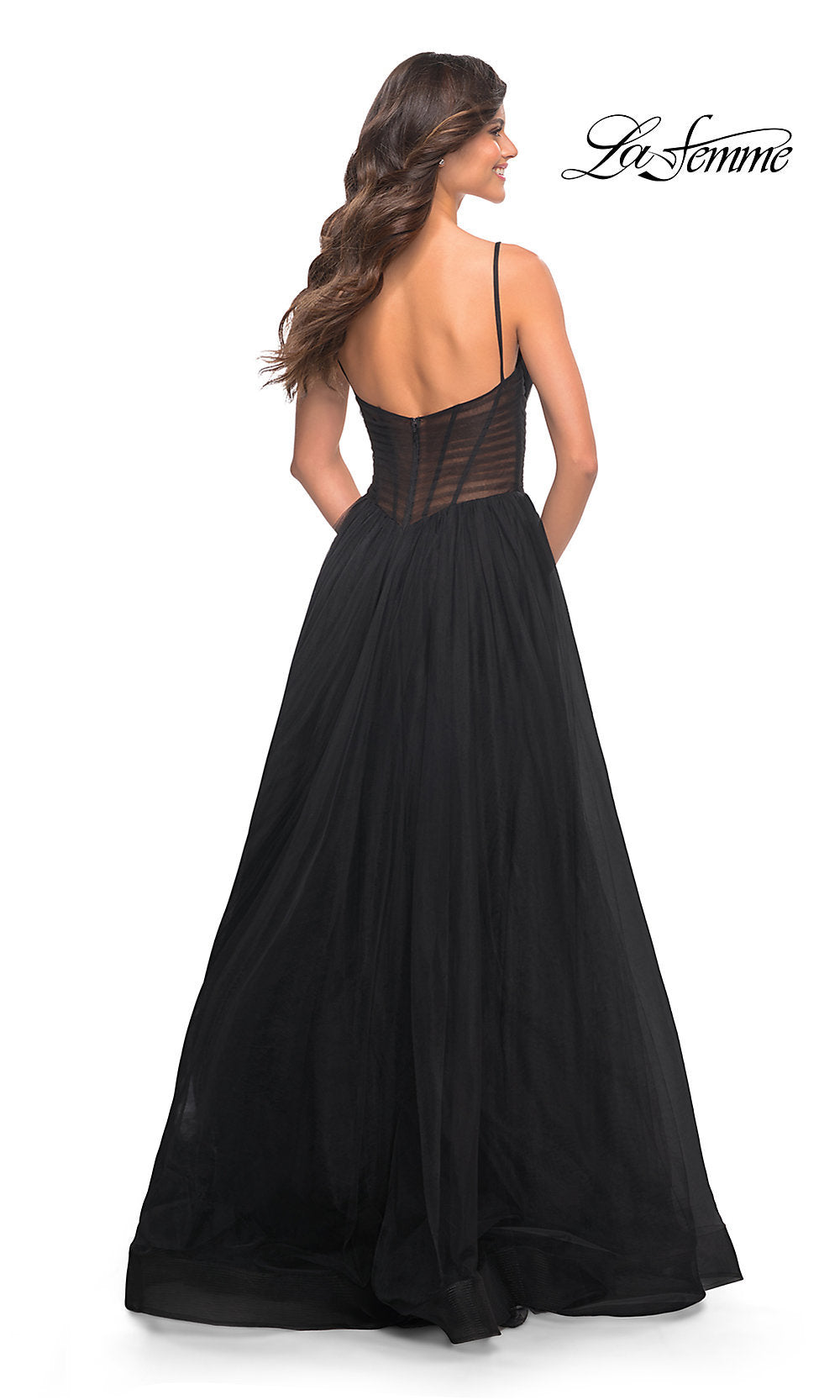 A woman faces away in a long black La Femme Prom Dress with thin straps and a sheer corset waist, on a white background. The